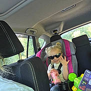 Ella joined the competition — help win amazing prizes! child, car_seat, sunglasses, blonde_hair, toy, car_interior, water_bottle, seatbelt, window, sunlight, road_trip, pink, gray, clothing, person, smiling, hair, seat, book, happy