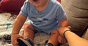 Joseph joined the competition — help win amazing prizes! baby, bed, blanket, blue_onesie, casual, child, couch, curious, expression, footwear, furniture, hand_holding, indoor, person, red_pillow, room, sci_fi, sitting, sneakers, young_child