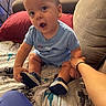 Joseph joined the competition — help win amazing prizes! baby, child, blue_onesie, sitting, bed, blanket, sci_fi, hand_holding, red_pillow, couch, indoor, person, footwear, sneakers, curious, expression, furniture, room, young_child, casual