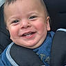 baby, smiling, face, child, stroller, blue_clothing, happy, outdoor, people, crowd, person, infant, teeth, head, seatbelt, urban, daylight, cute, closeup, portrait