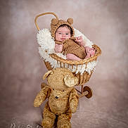 Myliano participe au concours pour gagner de l'argent avec cette photo : baby, infant, knitted_clothing, bear_ears, wicker_basket, plush_toy, teddy_bear, soft_fabric, portrait, studio_photography, child, cute, smiling, cozy, warm_lighting, neutral_background, fuzzy_texture, seated, small_hands, baby_feet