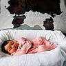baby, newborn, sleeping, pink_outfit, blanket, basket, fur_rug, cowhide, soft_texture, cozy, indoor, infant, peaceful, cute, child, portrait, resting, warm, comfortable, closeup