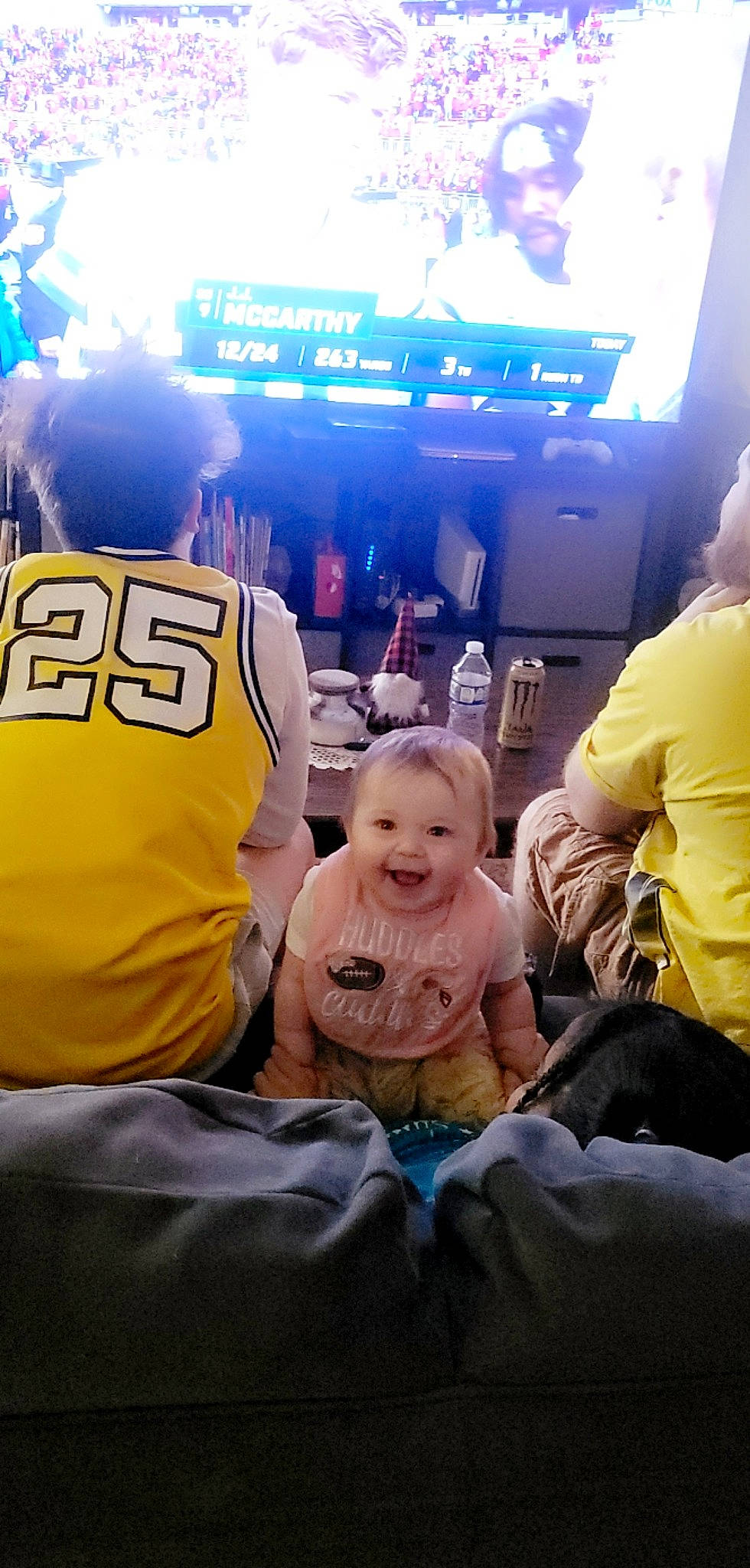 Makenzie is registered to the contest to win money with this photo: baby, child, crowd, event, fan, fun, happy, hat, joy, leisure, luxury_vehicle, people, person, recreation, room, sitting, t_shirt, team, television, toddler