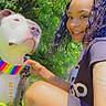 casual_clothing, crouching, curly_hair, daylight, dog, friendship, grass, greenery, happy, leash, nature, outdoor, pet, portrait, rainbow_collar, smile, summer, sunlight, tattoo, woman