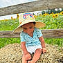 toddler, child, hat, straw_hat, blue_shirt, shorts, barefoot, hay, hay_bale, fence, sunflower, flower_field, outdoor, grass, summer, nature, portrait, sitting, sunny, rural