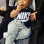 Jeremias is registered to the contest to win money with this photo: toddler, child, car_seat, clothing, hat, cap, nike, jeans, sock, footwear, indoor, person, baby, cute, curly_hair, expression, seat, sitting, hand, face