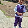 child, boy, outdoor, sunny, vest, bow_tie, purple_clothing, pants, shoes, standing, serious_expression, sidewalk, park, bench, daylight, portrait, young_child, casual, fashion, person
