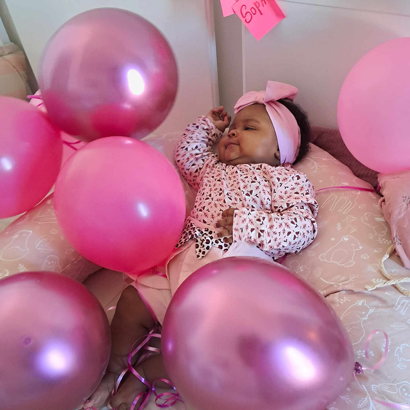 Kéren-Sophie participe au concours pour gagner de l'argent avec cette photo : baby, balloons, bed, celebration, child, cute, decor, footwear, headband, indoor, infant, patterned_clothing, person, pillow, pink, relaxing, ribbons, smiling, soft_furnishing, toddler