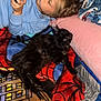 child, cat, gaming_device, blanket, cushion, spiderman, indoor, relaxing, playing, pet, black_cat, curly_hair, blue_sweatshirt, toy, comfort, resting, home, casual, young_person, leisure