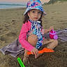 barefoot, beach, bucket_hat, child, curly_hair, nature, outdoor, play, recreation, sand, sand_toys, sea, shovel, sky, sunset, sunsuit, towel, toy, vacation, watering_can