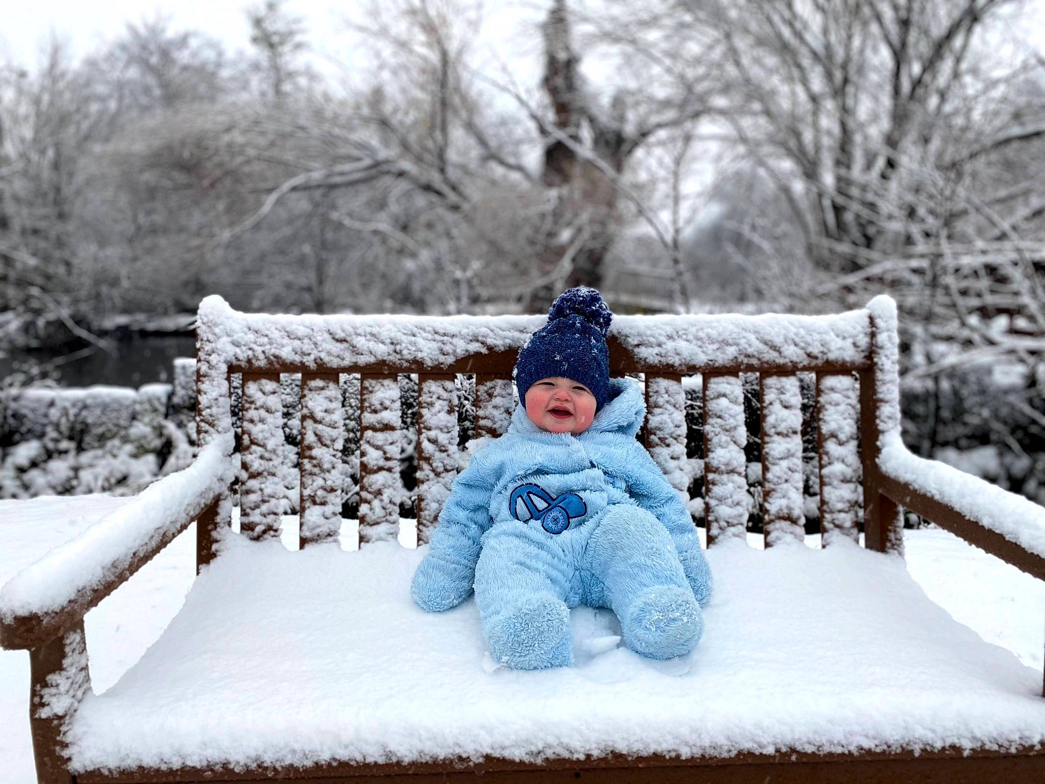 Gatlin is registered to the contest to win money with this photo: baby_toddler_clothing, beanie, bench, blizzard, bonnet, cheek, comfort, freezing, frost, headwear, hood, knit_cap, outdoor_furniture, person, playing_in_the_snow, portrait_photography, precipitation, sitting, snow, winter