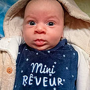 Soan participe au concours pour gagner de l'argent avec cette photo : baby, infant, face, eyes, hood, clothing, blue_outfit, embroidery, text_on_clothing, blanket, warm, cozy, portrait, cute, young_child, indoor, soft_texture, button, expression, person