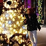bear, child, city, decoration, display, festive, footwear, hat, holding, holiday, illumination, jacket, lights, night, outdoor, sidewalk, smiling, toy, walking, winter_clothing