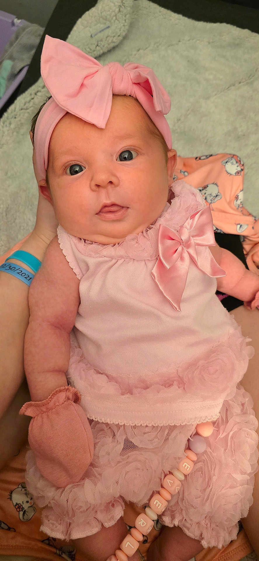 Everleigh is registered to the contest to win money with this photo: baby, infant, pink_clothing, headband, mitten, bracelet, beads, person, hand, closeup, portrait, cute, soft_fabric, patterned_blanket, indoor, human, newborn, wearing, accessory, holding