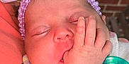 Everleigh is registered to the contest to win money with this photo: baby, sleeping, pacifier, headband, flower, hand, infant, closeup, skin, face, peaceful, child, cute, resting, newborn, window, brick_wall, clothing, purple, soft