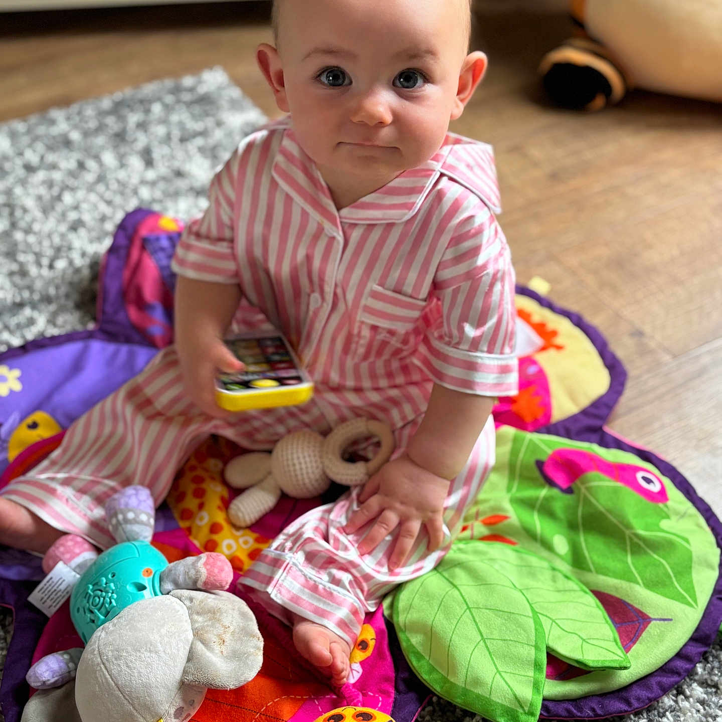 Harper is registered to the contest to win money with this photo: baby, carpet, child, colorful, cute, expression, floor, foot, hand, indoor, looking, pajamas, person, play_mat, sitting, soft_toys, striped_clothing, stuffed_animal, toys, wooden_floor