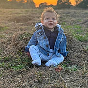 Otto is registered to the contest to win money with this photo: baby, child, denim_jacket, grass, sunset, outdoor, smiling, curly_hair, nature, field, clothing, happy, sitting, person, portrait, casual_wear, blue_eyes, daylight, young_child, scenery
