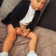 Cameron participe au concours pour gagner de l'argent avec cette photo : child, kid, boy, curly_hair, blazer, white_shirt, shorts, white_sneakers, socks, couch, blanket, indoor, portrait, seated, casual, fashion, accessory, bracelet, necklace, thoughtful