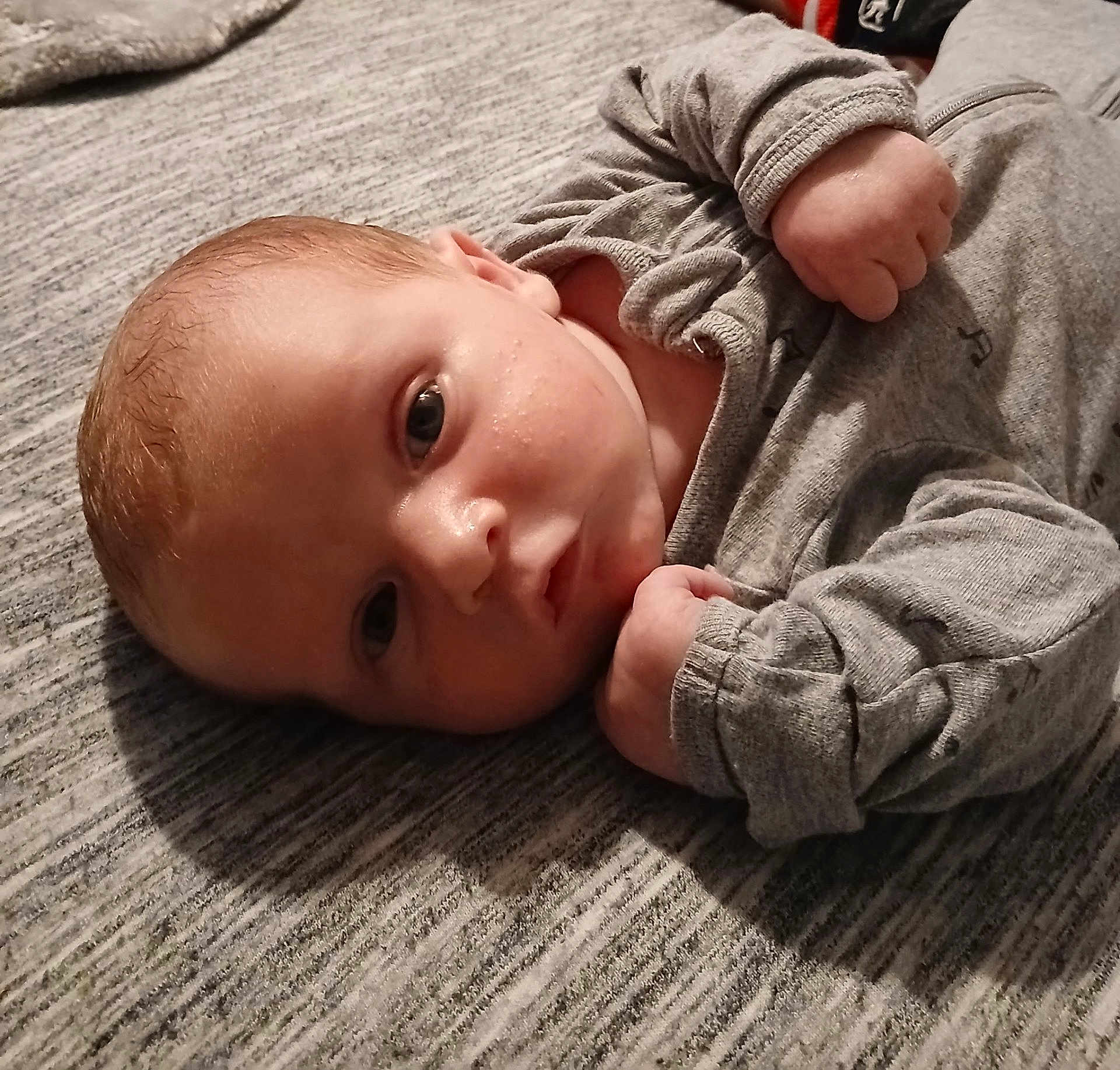 Gabriel Michael joined the competition — help win amazing prizes! baby, infant, face, person, clothing, grey_outfit, lying_down, fist, skin, head, eyes, indoors, soft_surface, texture, cute, young_child, portrait, expression, newborn, sleepwear