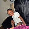 Jamir joined the competition — help win amazing prizes! toddler, child, smiling, indoor, couch, blanket, diaper, white_shirt, black_cover, purple_blanket, person, happy, furniture, home, door, light_switch, wall, foot, seated, portrait