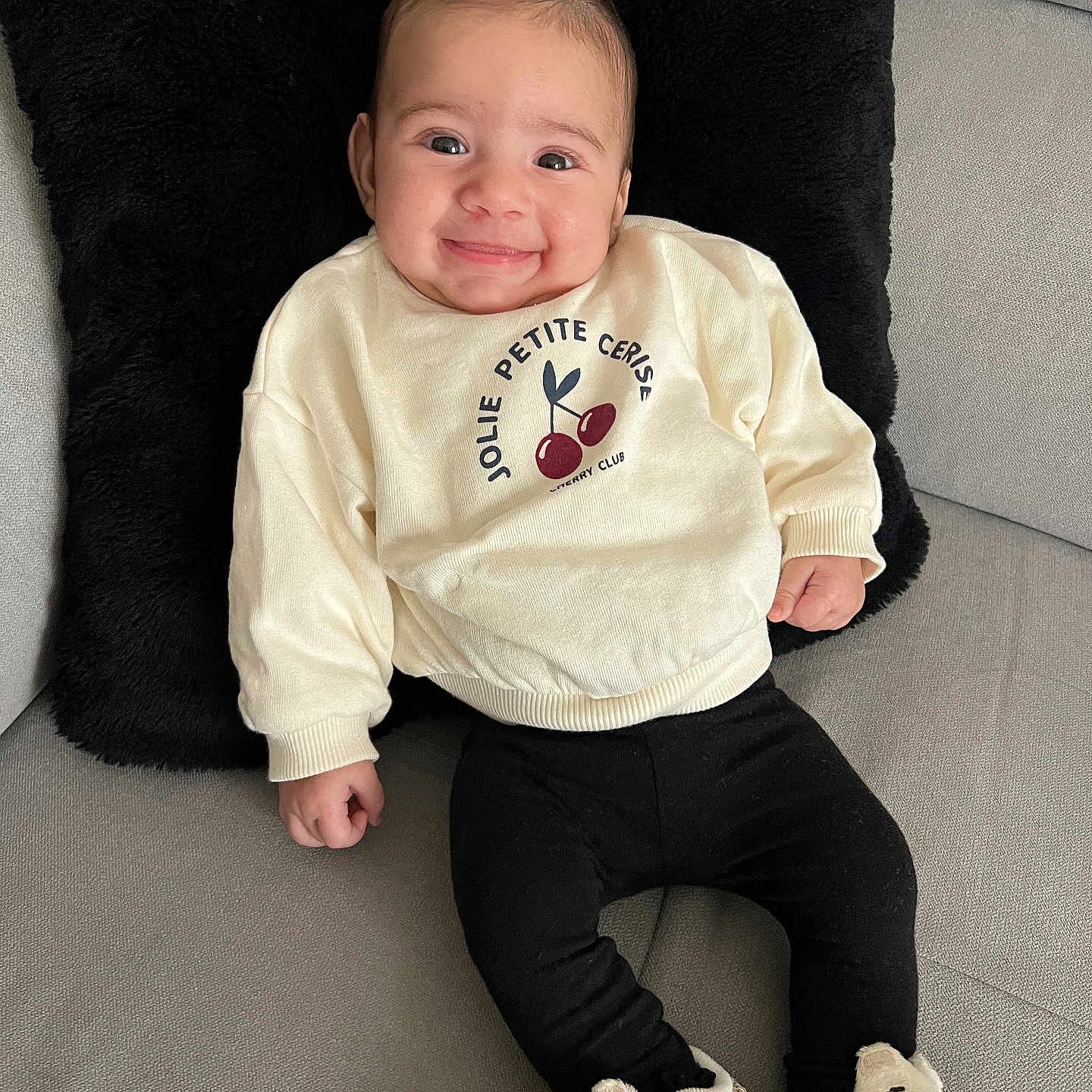 Naely a rejoint le concours — aidez-le/la à gagner de superbes lots ! apparel, baby, black_pillow, cherries, child, comfortable, couch, cute, footwear, happy, indoors, infant, leggings, person, plush, portrait, seated, smiling, sneakers, sweater