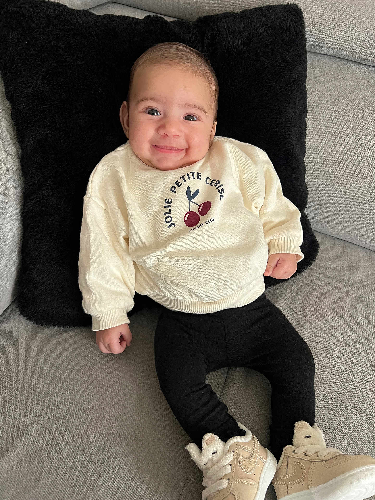 Naely a rejoint le concours — aidez-le/la à gagner de superbes lots ! apparel, baby, black_pillow, cherries, child, comfortable, couch, cute, footwear, happy, indoors, infant, leggings, person, plush, portrait, seated, smiling, sneakers, sweater