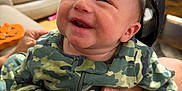 Frankie joined the competition — help win amazing prizes! baby, smile, camouflage_clothing, cap, tattoo, hand, living_room, sofa, couch, person, infant, happy, child, clothing, sitting, indoor, face, headwear, holding, cute