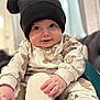 baby, child, hat, pom_poms, teddy_bear_print, clothing, sitting, seat, indoor, cute, face, hands, smile, cozy, soft_lighting, portrait, infant, apparel, expression, young