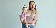 Emiliya is registered to the contest to win money with this photo: woman, baby, child, holding, portrait, indoor, casual_clothing, jeans, pink_top, long_hair, pony_tail, barefoot, light_background, minimalistic, mother_and_child, curious_expression, blue_eyes, human, family, gentle_lighting