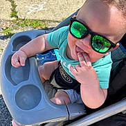 Ezekiel joined the competition — help win amazing prizes! baby, baby_bottle, casual, child, clothing, daylight, face, fingers, foot, green_tshirt, hand, happy, outdoor, person, playful, reflection, seat, stroller, sunglasses, sunny