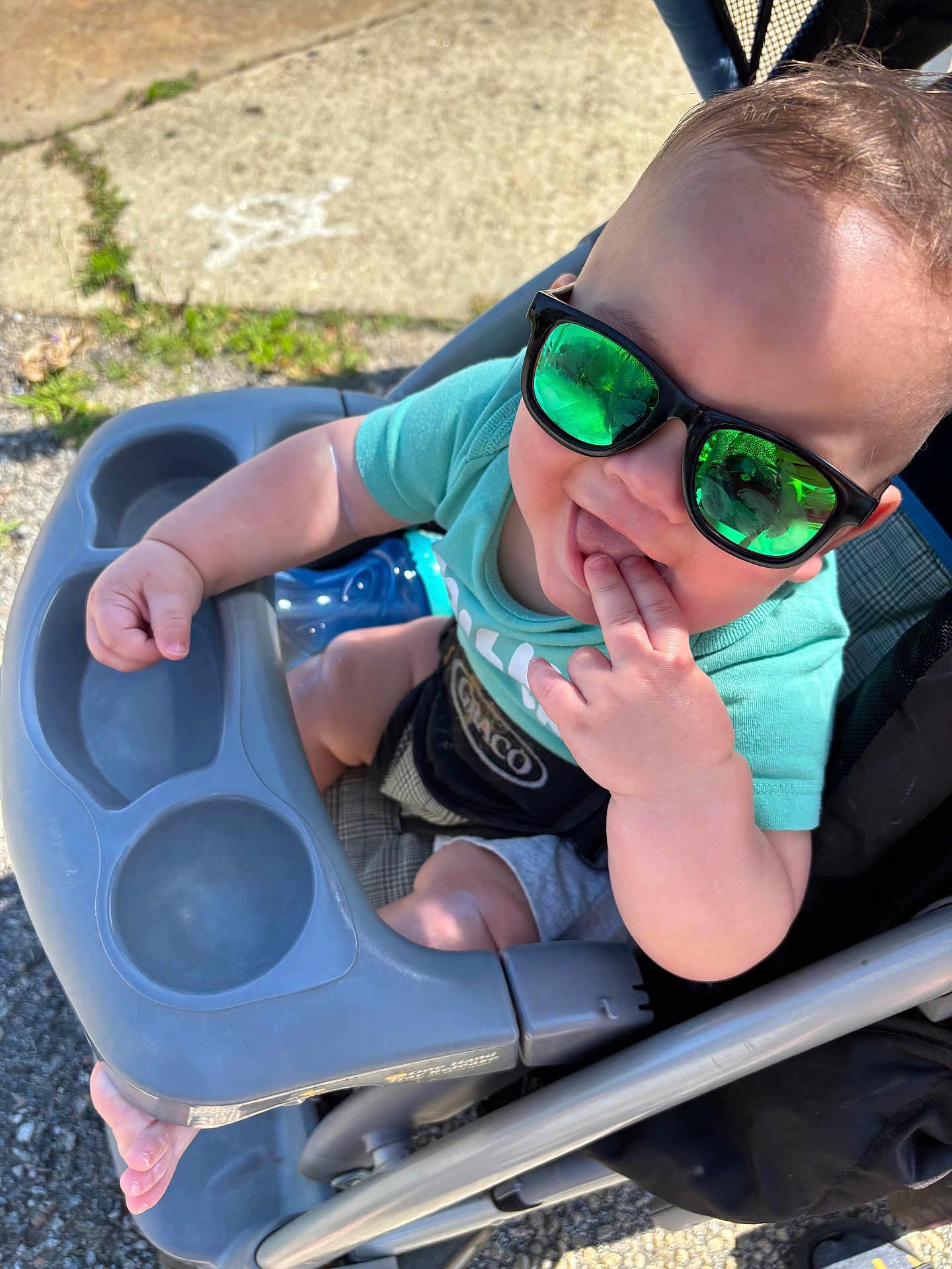Ezekiel joined the competition — help win amazing prizes! baby, baby_bottle, casual, child, clothing, daylight, face, fingers, foot, green_tshirt, hand, happy, outdoor, person, playful, reflection, seat, stroller, sunglasses, sunny