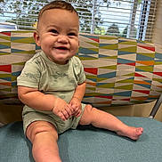 Ezekiel is registered to the contest to win money with this photo: baby, child, smiling, sitting, indoor, chair, patterned_fabric, window, blinds, natural_light, cute, happy, infant, legs, feet, shorts, tshirt, face, skin, person