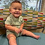 baby, child, smiling, sitting, indoor, chair, patterned_fabric, window, blinds, natural_light, cute, happy, infant, legs, feet, shorts, tshirt, face, skin, person