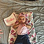 baby, infant, blanket, bed, bedding, headband, pink, bib, onesie, socks, towel, patterned_blanket, portrait, lying_down, cute, eyes, hands, comforter, quilt, pillow
