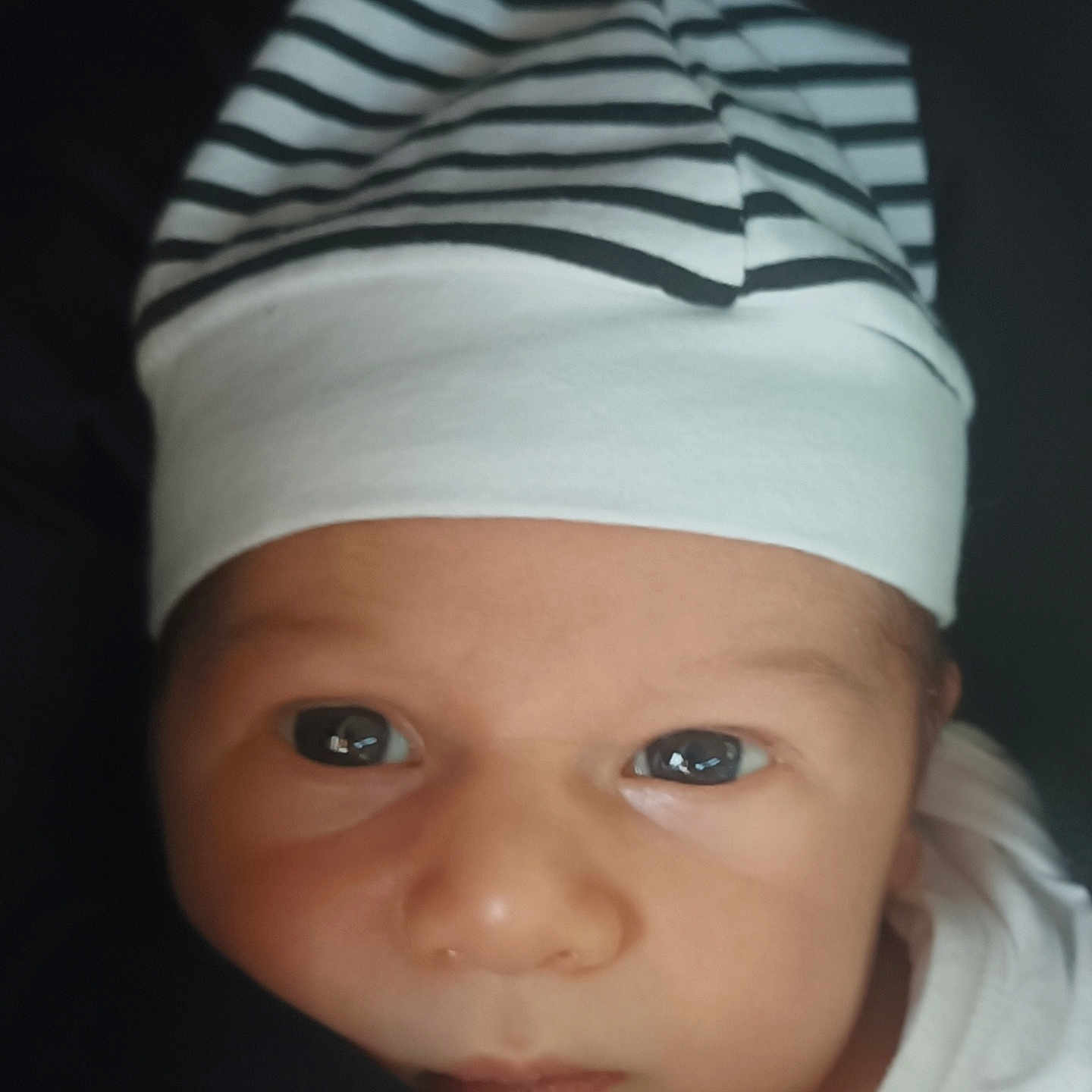 Evenn participe au concours pour gagner de l'argent avec cette photo : baby, black_background, child, closeup, cute, expression, eyes, face, hat, headwear, infant, newborn, newborn_baby, person, portrait, skin, soft_light, striped_hat, white_clothing, young_child