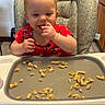 toddler, child, high_chair, pancakes, food, eating, red_shirt, kitchen, baby, smiling, face, person, seat, furniture, foot, hand, tray, snack, indoors, cute