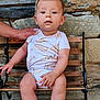 baby, child, bench, stone_wall, onesie, cap, hand, outdoor, cute, person, infant, wood, support, sitting, face, legs, skin, expression, casual, daylight