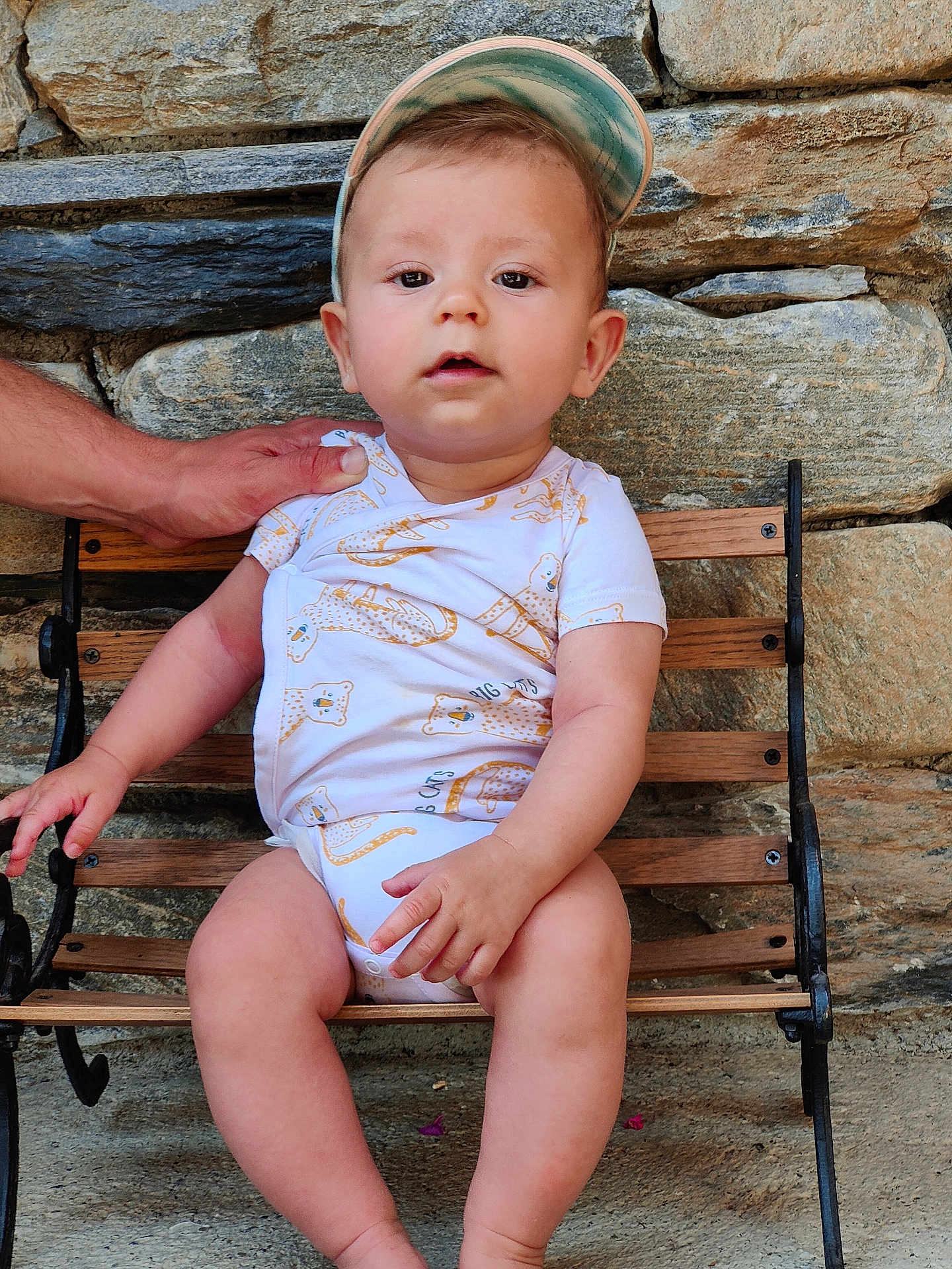 Leon participe au concours pour gagner de l'argent avec cette photo : baby, child, bench, stone_wall, onesie, cap, hand, outdoor, cute, person, infant, wood, support, sitting, face, legs, skin, expression, casual, daylight