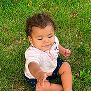 Ky'Ran joined the competition — help win amazing prizes! baby, child, infant, sitting, grass, outdoor, park, portrait, curly_hair, brown_hair, barefoot, smiling, curious, reaching, hand, pink_shirt, shorts, lawn, leaves, natural_light