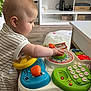 baby, child, toy, activity_table, indoor, living_room, furniture, television, carpet, floor, striped_clothing, hand, face, head, playing, colorful, plastic, learning, early_childhood, curious