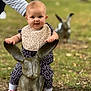 baby, child, statue, rabbit, outdoor, grass, bib, shoes, person, hand, nature, toy, play, park, cute, smile, footwear, animal_statue, ground, daylight