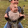 child, baby, smiling, outdoor, toy, rabbit_sculpture, playful, happy, grass, nature, sibling, cute, portrait, clothing, bib, jeans, striped_shirt, flower_pattern, daylight, playground