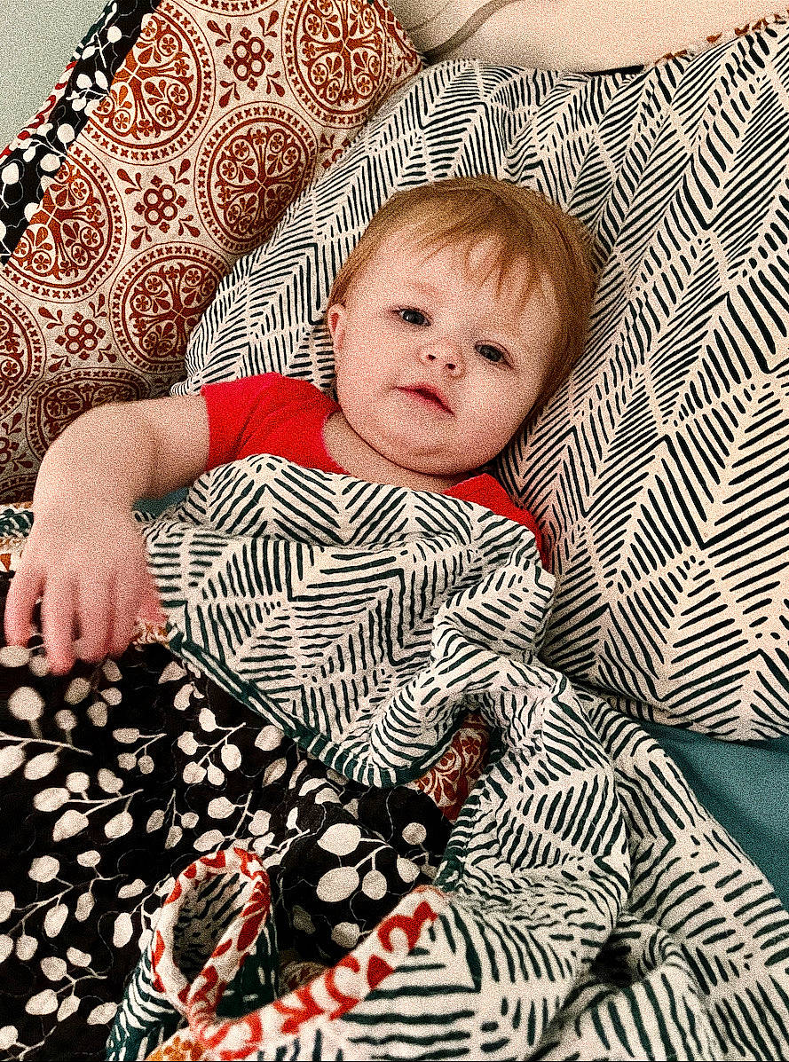 Leah is registered to the contest to win money with this photo: baby, baby_toddler_clothing, beauty, child, comfort, couch, facial_expression, human, linens, mammal, organ, pattern, people, person, product, room, sitting, sleeve, t_shirt, textile