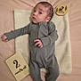 baby, infant, newborn, lying_down, blanket, milestone_card, gray_onesie, soft_texture, curious_expression, face, head, hand, foot, skin, person, indoor, bed, sleepwear, cute, two_months