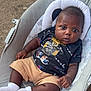baby, infant, child, sitting, cushion, baby_seat, outdoor, concrete, shorts, tshirt, socks, dark_skin, cute, portrait, looking_at_camera, casual_clothing, relaxed, small_hands, footwear, young_child