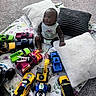 baby, blanket, carpet, child, clothing, colorful, cute, floor, happy, indoor, infant, pillow, play, playtime, plush, room, sitting, smile, toy_cars, young_child