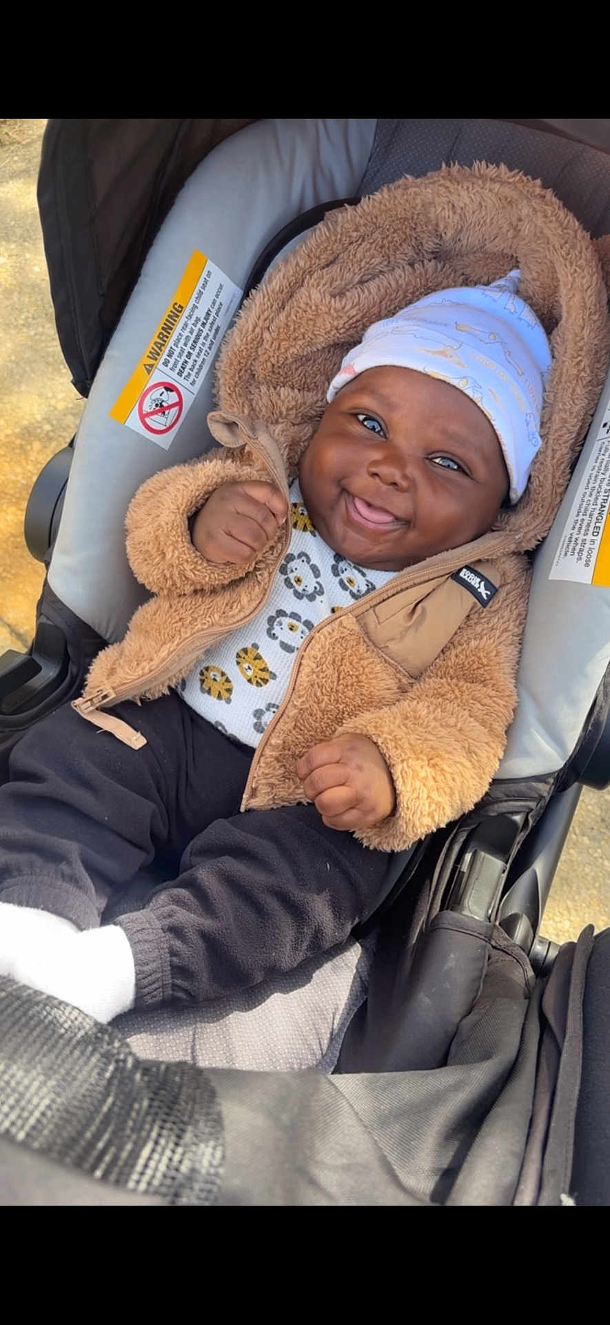 Legend is registered to the contest to win money with this photo: baby, smiling, child, stroller, jacket, hat, animal_print, pants, white_socks, happy, outdoor, infant, cute, cozy, fuzzy_clothing, portrait, seat, baby_clothing, baby_accessory, infant_smile