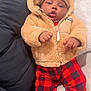 baby, child, hoodie, teddy_bear, plaid_pants, red_pants, couch, indoor, cozy, warm_clothing, socks, cute, infant, relaxed, portrait, person, face, hands, seated, blanket