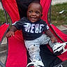 baby, black_shirt, casual, chair, child, clothing, cute, daylight, footwear, grass, happy, jeans, outdoor, person, portrait, red_chair, sitting, smiling, sneakers, toddler