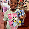 child, girl, smile, indoor, toy, bluey, tshirt, cartoon, hair_beads, wood_floor, photograph, family_photo, furniture, colorful, bracelet, packaging, bubble_wand, happy, person, portrait